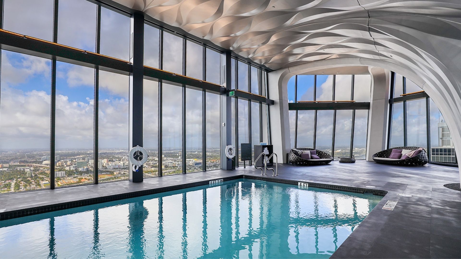 Large spacious living room with all white interior, glass coffee table, and outdoor seating facing the beautiful Biscayne Bay at Monad Terraces